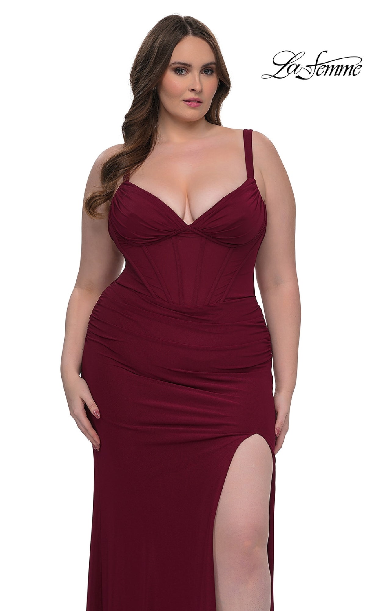 A woman models the Plus-Size Long Corset Prom Dress: La Femme 33015, a form-fitting, sleeveless burgundy gown with a thigh-high slit, posing against a white background. The